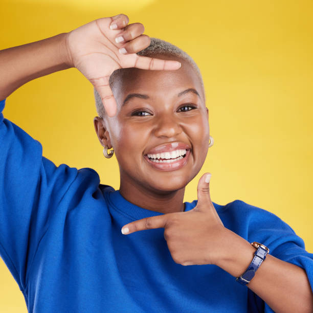 istock Portrait, frame and hand gesture with a black woman in studio on a yellow background feeling happy. Hands, smile and focus with an attractive young female finger framing her face against a color wall 1494324569