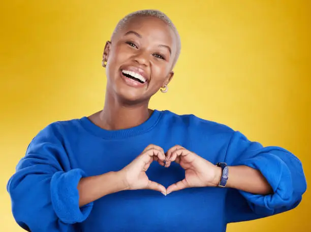 Photo of Heart hands, portrait and happy black woman in studio, background and color backdrop for emoji. Smile, female model and finger shape for love, thank you and support of peace, care or sign of kindness