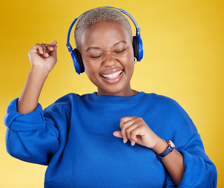 Music, headphones and black woman dance in studio isolated on a yellow background. Podcast, radio and happy African female streaming, enjoying and listening to audio, sound track or song for dancing.