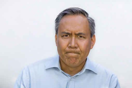 Portrait of Asian Chinese mixed race senior mature man in collared business shirt making a frustration face looking at camera