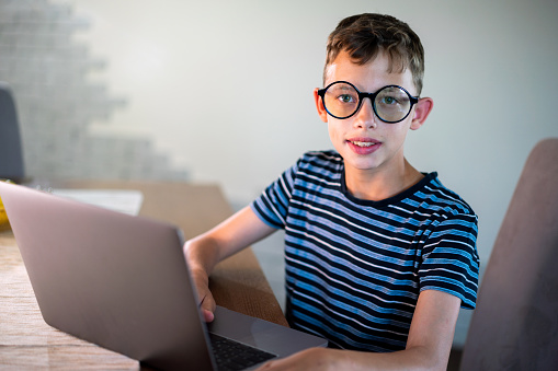 Portrait of a teenage boy whit eyeglasses using laptop at home