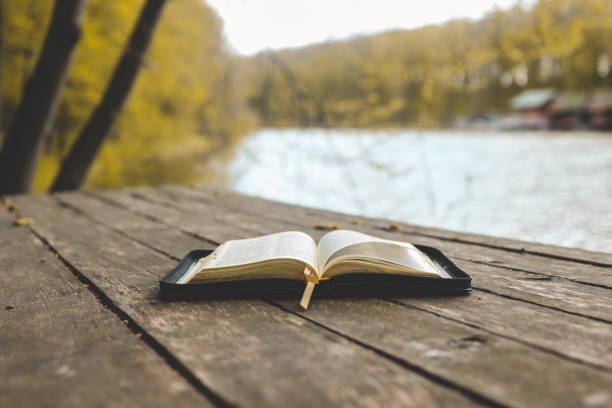 istock Open Bible on a wooden board near the river 1494325501