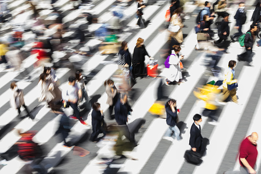 picture with intentional motion blur of crowds of people who are crossing a city street at a zebra crossing in Tokyo, Japan