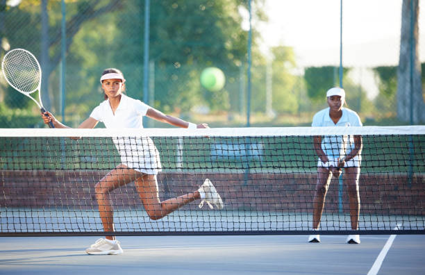 tennis, fitness und eine sportlerin, die während eines wettkampfspiels einen ball über ein netz schlägt, um einen aufschlag zurückzugeben. bewegung, gesundheit oder training mit einer athletin und einem doppelpartner, die auf einem platz spielen - doubles stock-fotos und bilder