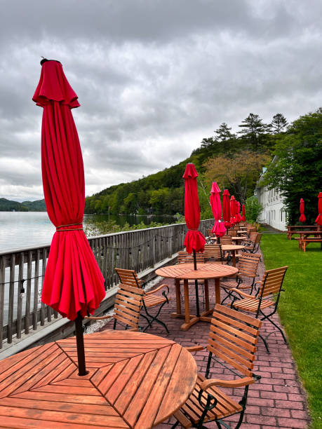 lakeside picnic tables (overcast cloudy skies) closed red umbrella, chairs, railing, water, mountains (scenic dining)