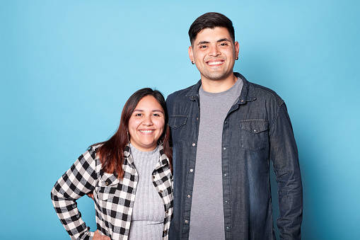 Young latin couple smiling looking at camera isolated on blue background. Copy space.
