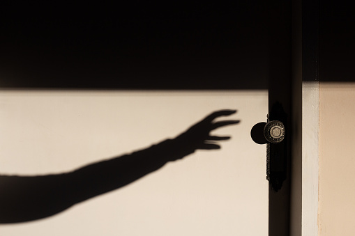 Goiania, Goias, Brazil – May 17, 2023: The shadow of an arm with a hand trying to open a closed white door.