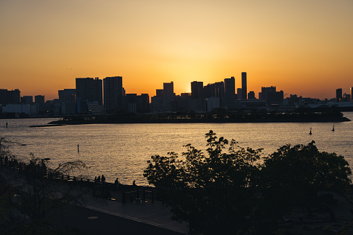 view from Odaiba, Tokyo, over the bay to the skyline of Tokyo at sunset with silhouettes of unrecognizable people in the foreground