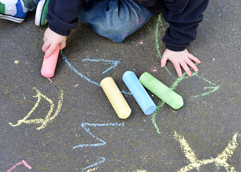 Closeup of a two year old boy playing with sidewalk chalk on pavement.