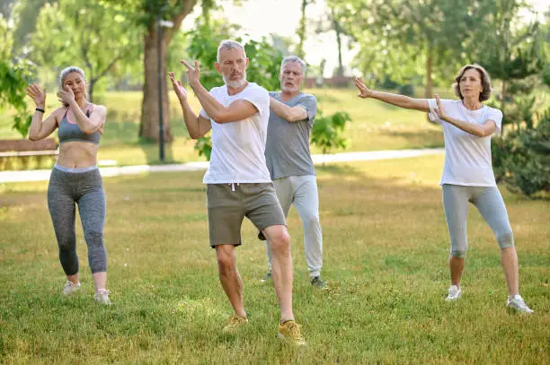 A group of people practicing qigong in a park, sport workout in nature.