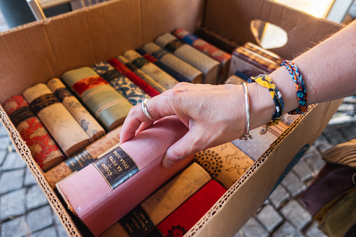 Detail of a woman'hand picking up a old used book among others in a box at an outdoor flea market, Italy.