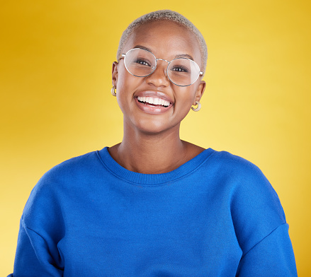 Young black woman, studio portrait and smile with glasses, eye health or fashion frame by yellow background. African, student girl or model for happiness, youth or beauty with eyes, vision and happy