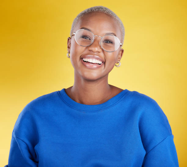young black woman, studio portrait and smile with glasses, eye health or fashion frame by yellow background. african, student girl or model for happiness, youth or beauty with eyes, vision and happy - nature beauty women fashion model imagens e fotografias de stock