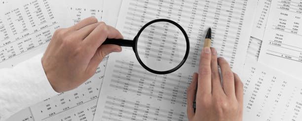 Woman holding a magnifying glass pointing at numbers on financial documents. ?oncept of finance, search and accounting. stock photo