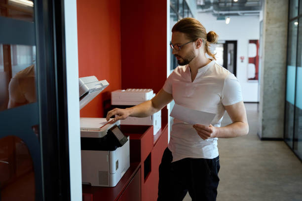 Handsome male worker using multifunction printer indoors stock photo