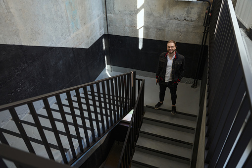 Attractive male in glasses put his hand in his pocket while looking at camera on stairwell