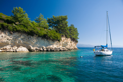 The crystal clear waters of the bay of Loggos, with a yacht at anchor in the beautiful bay near the village: Paxos, Greece