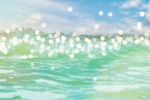 Close-up of the sea wave with the foam surging on the shore. Background with bright splashes and bokeh on the theme of a dream vacation.