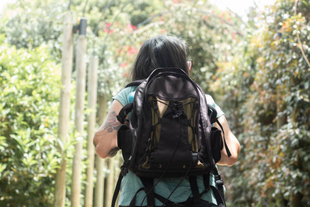 Backside view of a woman wearing a backpack and walking through lush foliage