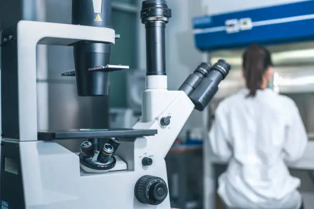 Photo of Inverted microscope and a female scientist working at the laboratory.