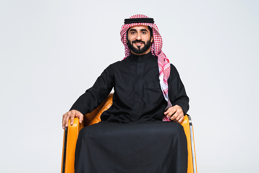 Handsome arab middle-eastern man with traditional saudi clothing in studio - Arabic muslim adult male businessman wearing thwab portrait isolated on gray background