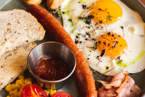 Fried eggs with sausages, tomato and bread on plate. English breakfast in cafe. Continental breakfast table. Eggs with meat and vegetables. Ready to eat food. Healthy dinner. Restaurant menu.