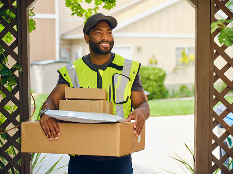 A professional delivery person at a home entry holding packages.