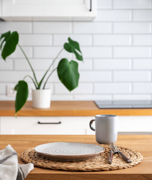 istock Wooden table top with plate and cup for breakfast against blurred white kitchen with cutting board and monstera plant in scandinavian style 1494364834