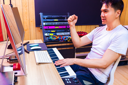 friendly asian male music producer enjoy arranging music on computer in home studio. music production concept