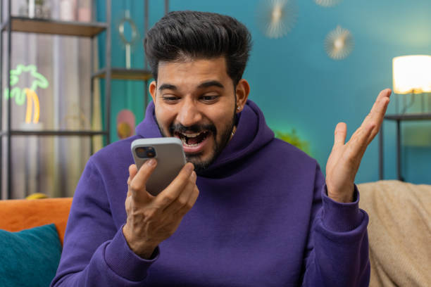 istock Happy indian man at home use smartphone typing browsing wow yes found out great big win celebrate 1494370068