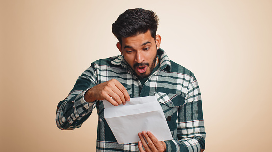 Handsome indian man open envelope take out letter reads it feel happy. Hindu guy career growth advance promotion, bank loan approve, monetary award, long-awaited invitation great news, lottery win