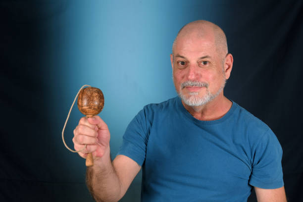 happy bald man with white beard playing with antique children's toy bilboquet looking forward with good expression