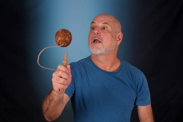 happy bald man with white beard playing with antique children's toy bilboquet looking forward with good expression