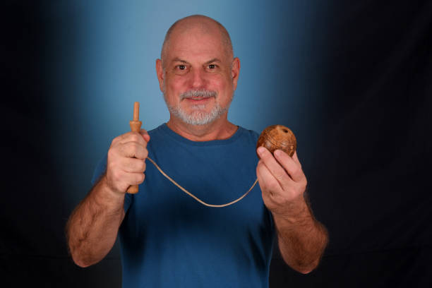 happy bald man with white beard playing with antique children's toy bilboquet looking forward with good expression