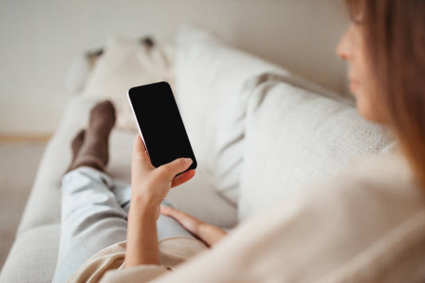 istock Serious millennial european female typing on phone with empty screen, sits on sofa, resting, enjoy spare time 1494372020