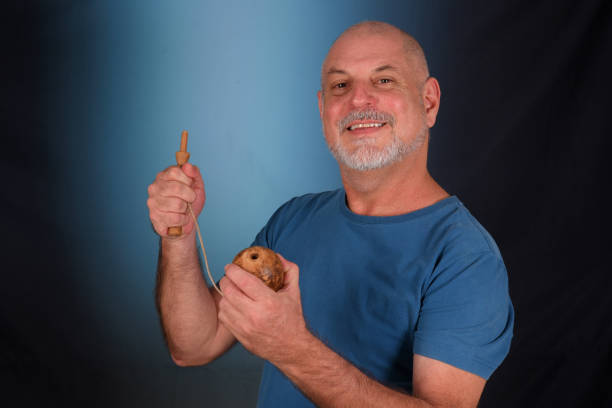 happy bald man with white beard playing with antique children's toy bilboquet looking forward with good expression