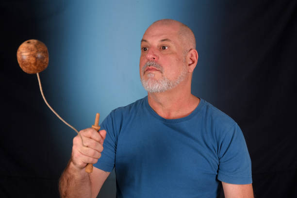 happy bald man with white beard playing with antique children's toy bilboquet looking forward with good expression