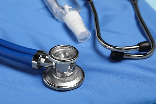 Stethoscope and antiseptic on light blue medical uniform, closeup