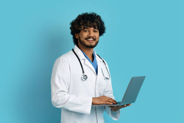 istock Cheerful hindu doc holding laptop, isolated on blue 1494372679