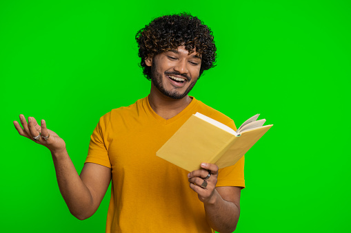 Happy indian man reading funny interesting fairytale story book, leisure hobby, knowledge wisdom, education, learning, study, wow. Handsome hindu guy isolated alone on green chroma key background