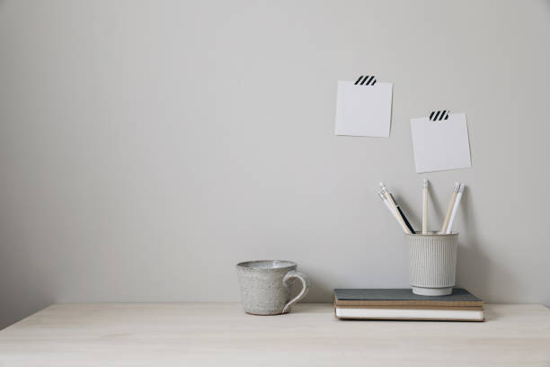 istock Office table. Empty desk with office supplies and beige wall copy space. Pencils holder, notebooks and cup of coffee. Blank note pad mockups, striped washi tape. Elegant interior, work break concept. 1494376633