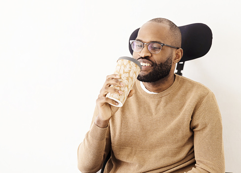 Black man in a wheelchair having coffee, using reusable cup
