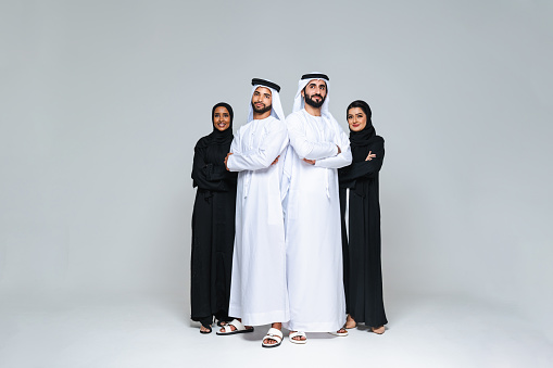 Beautiful arab middle-eastern women with traditional abaya dress and middle easter man wearing kandora in studio - Group of arabic muslim adults portrait in Dubai, United Arab Emirates