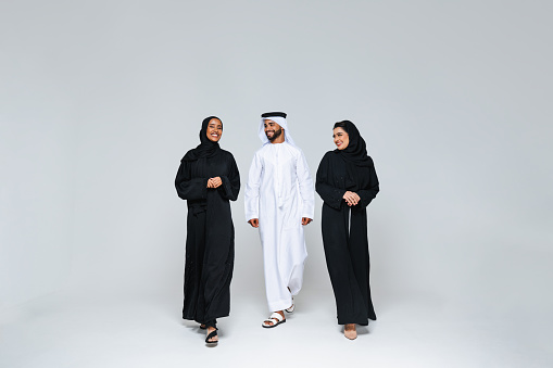 Beautiful arab middle-eastern women with traditional abaya dress and middle eastern man wearing kandora in studio - Group of arabic muslim adults portrait in Dubai, United Arab Emirates