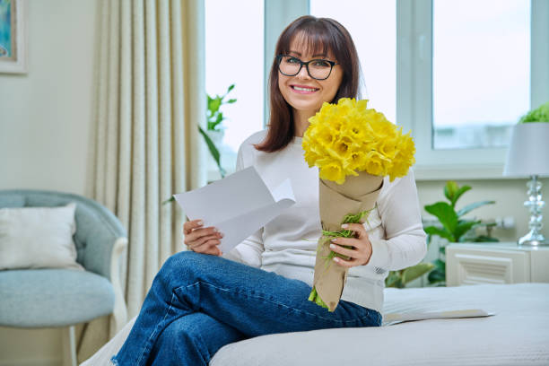 glückliche frau mittleren alters mit blumenstrauß, zu hause - love flower single flower letter stock-fotos und bilder