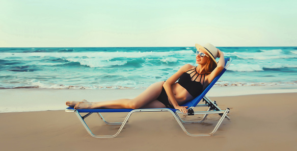 Summer vacation, happy relaxing young woman lying on deckchair on the beach on sea background