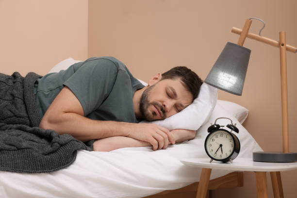istock Man sleeping in bed and alarm clock on nightstand at home 1494379701