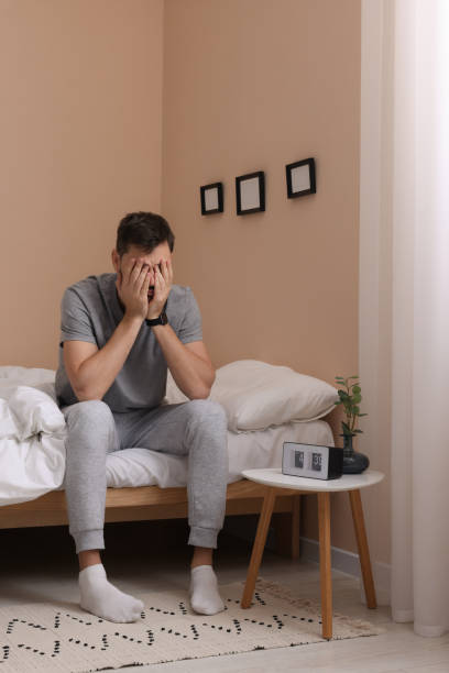 istock Sleepy man covering his face with hands on bed at home 1494379708