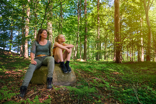 Enjoying forest nature together. Mother and daughter sitting in beautiful nature. Springtime with lush foliage