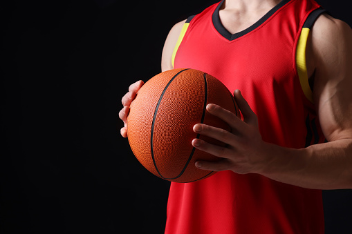 Athletic man with basketball ball on black background, closeup. Space for text